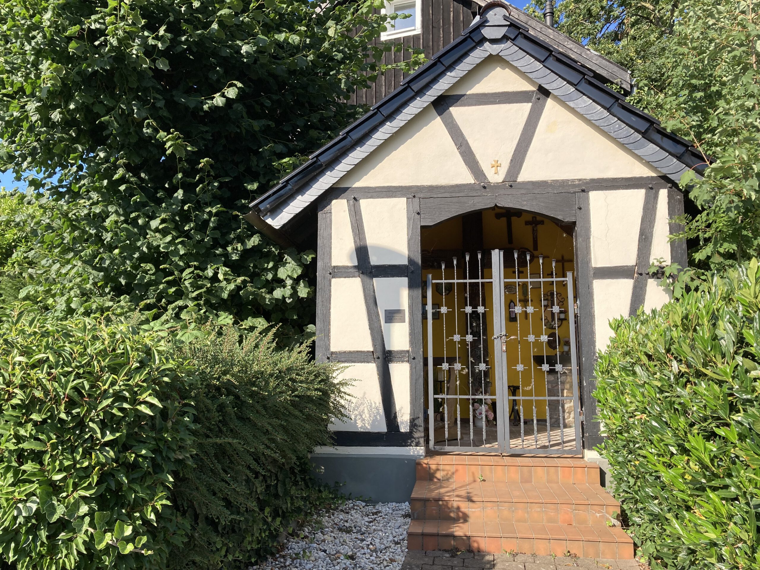 Kapelle in Geisbach mit geschlossenem Gittertor, die Sonne scheint.