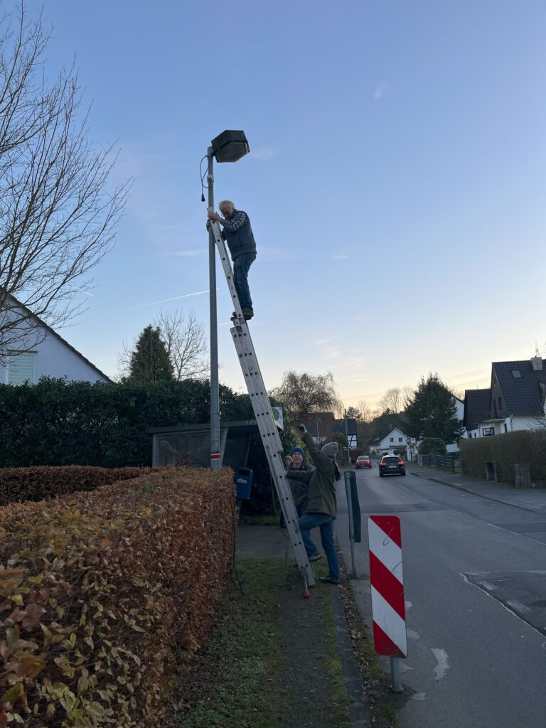 Ein Mann steht auf einer Leiter, die an eine Straßenlaterne gelehnt ist.